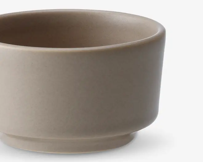 En rund skål med mat finish i en lys beige farve. Skålen har en glat overflade med en let tyk kant og en diskret fod, som giver den et stabilt udtryk. Det minimalistiske design og den neutrale tone gør den velegnet til forskellige borddækninger.