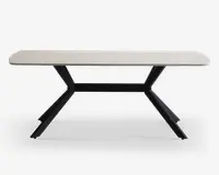 Et moderne, rektangulært bord med en lys, glat bordplade og afrundede hjørner. Bordet har karakteristiske sorte metalben, der vinkler udad i en V-form og giver et stabilt og stilfuldt fundament. Designet er minimalistisk og nutidigt, velegnet til forskellige indretninger.