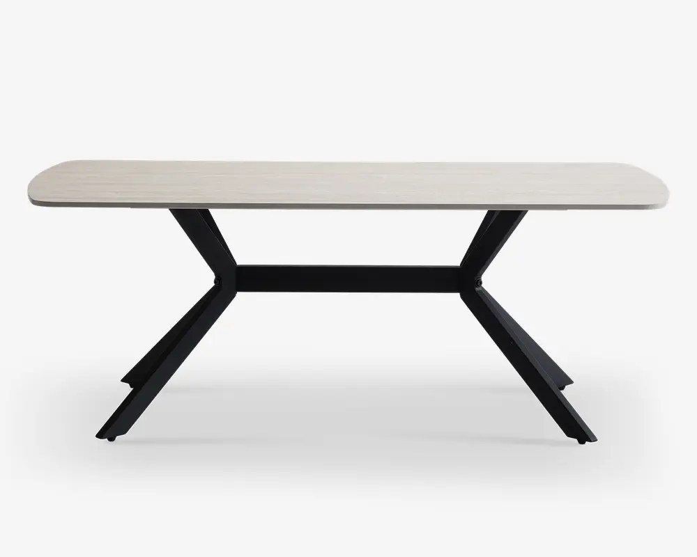 Et moderne, rektangulært bord med en lys, glat bordplade og afrundede hjørner. Bordet har karakteristiske sorte metalben, der vinkler udad i en V-form og giver et stabilt og stilfuldt fundament. Designet er minimalistisk og nutidigt, velegnet til forskellige indretninger.