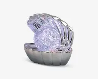 En dekorativ genstand formet som en åben muslingeskal med en blank, sølvfarvet overflade. Inde i skallen ligger en stor, rund kugle dækket af glitrende, iriserende farver, der ligner en perle. Designet er elegant og iøjnefaldende, velegnet til udstilling eller som en unik gave.