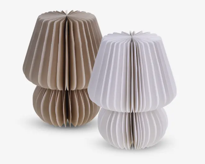 To dekorative genstande med plisseret, harmonika-lignende design, der minder om lampeskærme. Den ene er beige og den anden er hvid. Begge har en rundet bund og en bredere, udadbuet top, hvilket giver dem et skulpturelt og moderne udtryk. Materialet ligner kraftigt papir eller let pap, og genstandene kan stå frit.