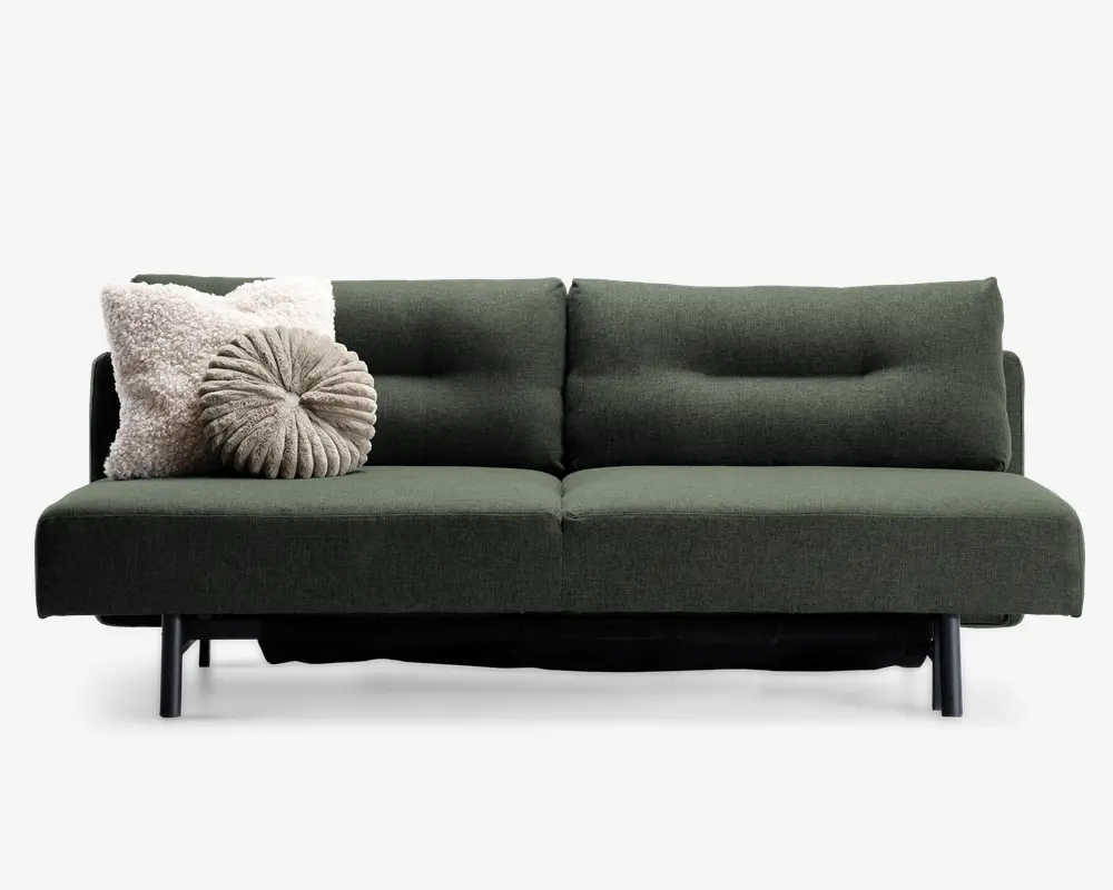 En moderne sofa med mørkegrønt betræk og minimalistisk design, med rene linjer og sorte metalben. Sæde- og ryghynderne har diskrete knapdetaljer, der giver ekstra struktur. To pyntepuder ligger i venstre side: en firkantet, cremefarvet og fluffy pude samt en rund, plisseret pude i en lys taupe farve.