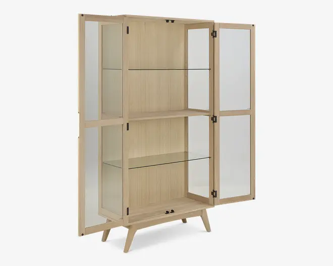 Høj vitrineskab med lys træramme, to glaslåger og glaspaneler på siderne. Indvendigt er der to klare glashylder til opbevaring eller udstilling, og skabet står på fire skråtstillede ben for et moderne udtryk. Lågerne har små runde greb, og designet er minimalistisk og elegant.