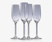 Sæt med fire klare glasfløjter med høje, slanke skåle og lange stilke. Hver glas har diskrete lodrette riller langs skålen, hvilket giver et elegant og tekstureret udtryk. Fodene er brede og flade for stabilitet.