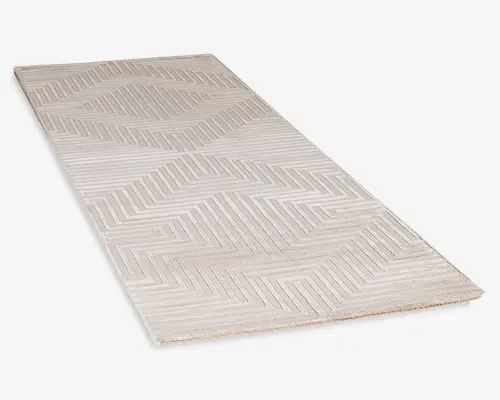 Rektangulært tæppe i en lys beige farve med et moderne geometrisk mønster bestående af chevron- og sildebenslinjer. Overfladen har en lav luv, hvilket giver et glat og fladt udtryk. Designet er minimalistisk og neutralt, velegnet til moderne indretning.