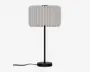En bordlampe med en hvid, plisseret stofskærm, en slank sort stamme og en rund sort fod, med ledningen synlig til venstre.