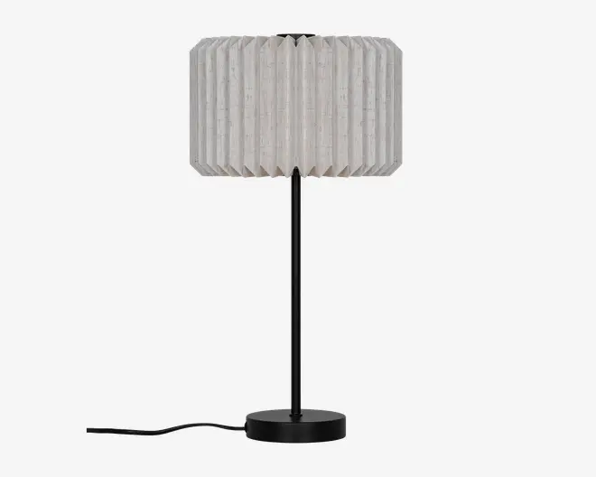 En bordlampe med en hvid, plisseret stofskærm, en slank sort stamme og en rund sort fod, med ledningen synlig til venstre.