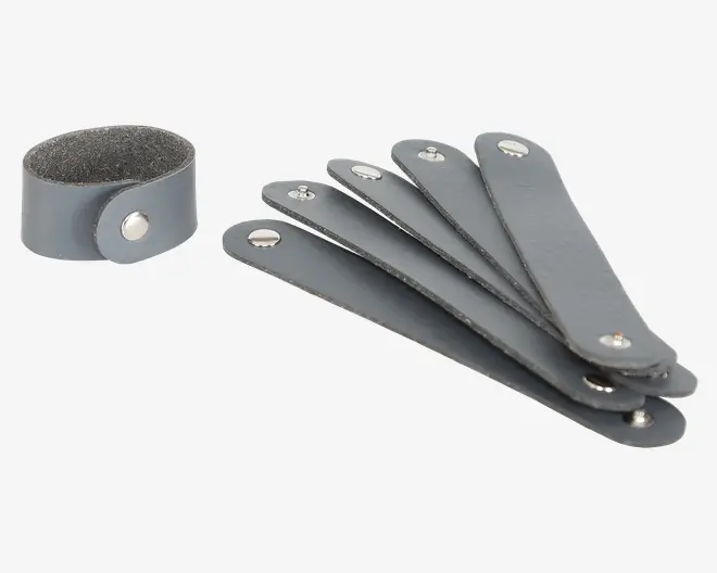 Sæt med fem grå kabelholdere i kunstlæder med sølvfarvede trykknapper. Hver rem er rektangulær med afrundede ender og en enkelt trykknap, så den kan vikles rundt om kabler eller ledninger for at holde dem organiseret. Materialet har en glat overflade udvendigt og en blød, filt-lignende inderside.
