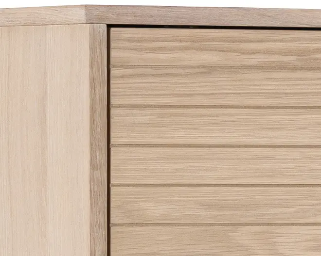 Nærbillede af et møbel i lyst egetræ med en glat, naturlig træstruktur. Frontpanelet har vandrette riller, som giver et moderne og tekstureret udtryk. Kanterne er rene og firkantede, hvilket understreger et minimalistisk design.