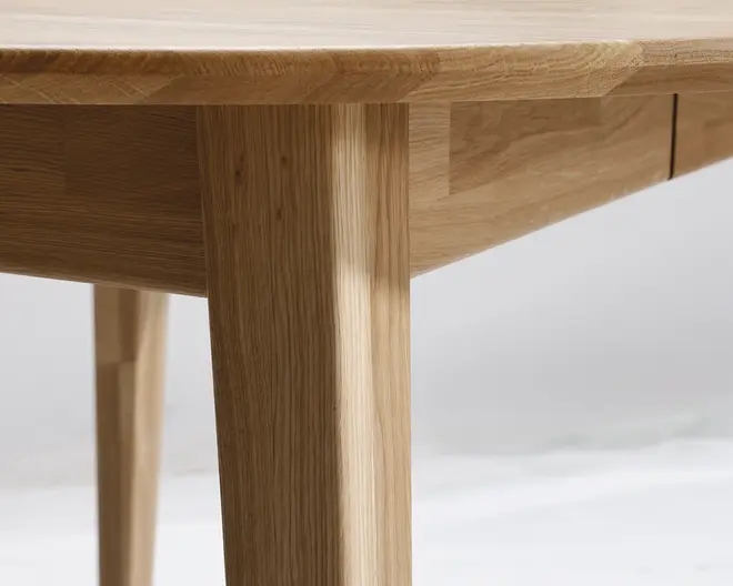 Nærbillede af et møbel lavet af lyst træ, der viser en glat, afrundet bordkant og solide, lige ben. Træets årer er synlige og fremhæver den naturlige struktur og finish. Konstruktionen fremstår robust med rene linjer og præcise samlinger.