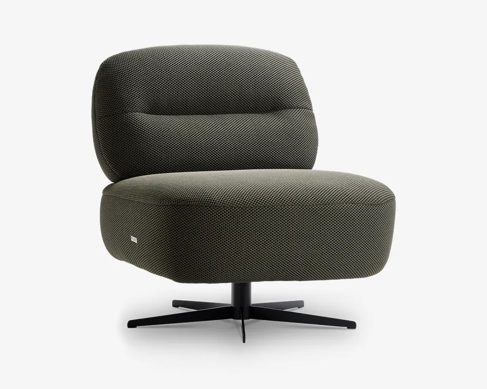 Moderne loungestol med afrundet, kraftigt polstret sæde og ryglæn, betrukket med et tekstureret mørkegrønt stof. Stolen har en lav profil og står på en sort, firebenet metalfod med drejefunktion, hvilket giver både komfort og stabilitet. Betrækket har et diskret vævet mønster, og et lille stofmærke ses på siden af sædet.