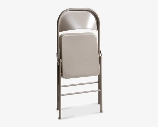En sammenklappelig stol i metal i en lys beige farve, vist i sammenfoldet tilstand. Stolen har et buet ryglæn og et fladt sæde, begge lavet af metal. Benene er lige med vandrette støttebøjler for ekstra stabilitet. Det kompakte design gør den nem at opbevare og transportere.
