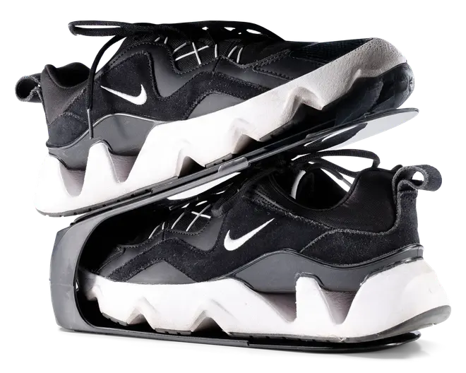 Par sorte og hvide sportssko med en kraftig, zigzag-mønstret hvid sål og sort overdel med ruskinds- og meshpaneler. Skoene har et lille hvidt swoosh-logo på siden, sorte snørebånd og en strop bagpå hælen. Skoene er vist stablet sål mod sål, hvilket fremhæver den tykke, skulpturelle mellemsål og den teksturerede ydersål.