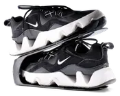 Par sorte og hvide sportssko med en kraftig, zigzag-mønstret hvid sål og sort overdel med ruskinds- og meshpaneler. Skoene har et lille hvidt swoosh-logo på siden, sorte snørebånd og en strop bagpå hælen. Skoene er vist stablet sål mod sål, hvilket fremhæver den tykke, skulpturelle mellemsål og den teksturerede ydersål.