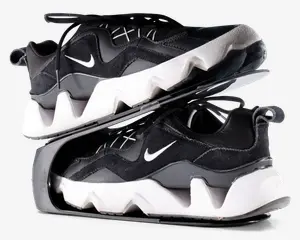 Par sorte og hvide sportssko med en kraftig, zigzag-mønstret hvid sål og sort overdel med ruskinds- og meshpaneler. Skoene har et lille hvidt swoosh-logo på siden, sorte snørebånd og en strop bagpå hælen. Skoene er vist stablet sål mod sål, hvilket fremhæver den tykke, skulpturelle mellemsål og den teksturerede ydersål.