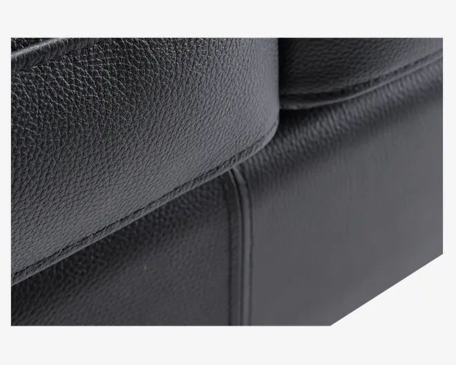 Nærbillede af en sort overflade i kunstlæder med en fin, nubret tekstur. Syningerne er tydelige og lige, hvilket vidner om god håndværksmæssig kvalitet. Materialet ser glat og let blankt ud, hvilket tyder på holdbarhed og nem rengøring.