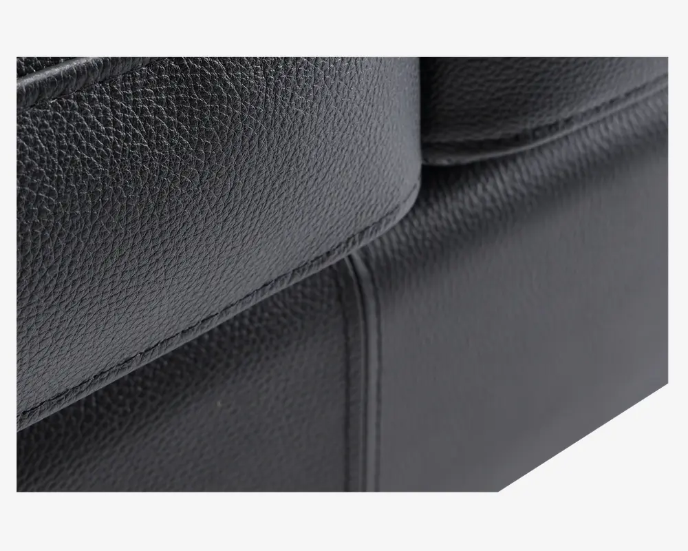 Nærbillede af en sort overflade i kunstlæder med en fin, nubret tekstur. Syningerne er tydelige og lige, hvilket vidner om god håndværksmæssig kvalitet. Materialet ser glat og let blankt ud, hvilket tyder på holdbarhed og nem rengøring.