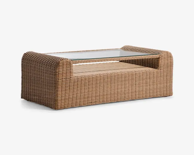 Rektangulært sofabord med en ramme i fletlook i en naturlig lys brun farve. Bordet har en klar glasplade, der ligger plant i rammen og giver en glat, rengøringsvenlig overflade. Sider og bund er fuldt indpakket i det samme flettede materiale, hvilket giver et ensartet og solidt udtryk. Hjørnerne er afrundede for et blødere udseende, og designet er moderne og egnet til både indendørs og udendørs brug.