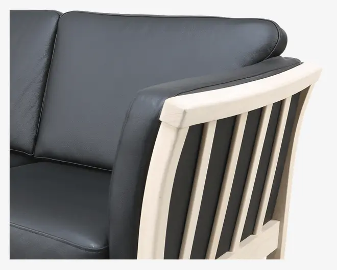 Nærbillede af et møbel med sorte læderhynder og en lys træramme. Ryglænet har lodrette trælameller, og armlænet er polstret med sort læder for ekstra komfort. Designet kombinerer moderne og klassiske elementer med glat polstring og en solid trækonstruktion.