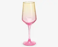 Et højt, elegant glas med lang stilk og bred skål. Glasset har et farveforløb, der går fra en lys gul øverst til en kraftig pink nederst. Skålen har diskrete lodrette riller, som giver ekstra struktur og visuel effekt.