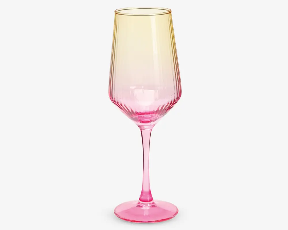 Et højt, elegant glas med lang stilk og bred skål. Glasset har et farveforløb, der går fra en lys gul øverst til en kraftig pink nederst. Skålen har diskrete lodrette riller, som giver ekstra struktur og visuel effekt.