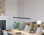 Et moderne, minimalistisk pendellampe med en lang, slank rektangulær form, ophængt fra loftet med to tynde sorte ledninger. Lampen har en mat sort finish med naturlige trædetaljer i enderne, hvilket giver et stilrent og nutidigt udtryk. Den er designet til at give jævn belysning over spisebordet nedenunder.