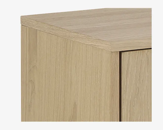 Nærbillede af et møbel med lys egetræsfinish, der viser rene linjer og en glat overflade. Hjørnekonstruktionen fremhæver det naturlige træmønster og den præcise samling mellem top- og sidepaneler.
