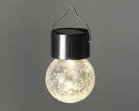 Hængende lampe med en rund glaskugle med krakeleret overflade, der udsender et varmt hvidt lys. Toppen består af en sort cylindrisk kappe med indbygget solcellepanel og et metalhåndtag til nem ophængning. Glaskuglen har en tekstureret, krakeleret finish, som får lyset til at glimte ekstra.