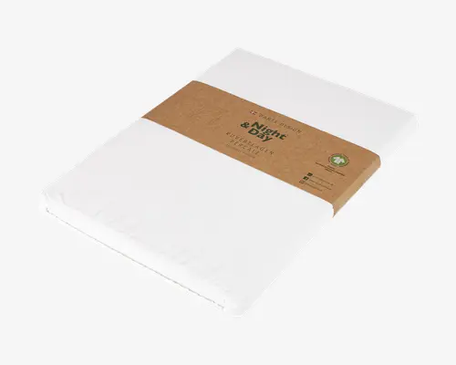 Et pænt sammenfoldet hvidt tekstilprodukt, pakket rektangulært med et brunt papirbånd omkring midten. Båndet har trykt tekst og miljøvenlige symboler, hvilket indikerer, at produktet er fremstillet af bæredygtige materialer. Emballagen er enkel og minimalistisk med tydelig mærkning og et naturligt, jordnært udtryk.