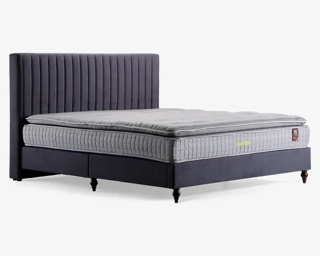 Moderne seng med høj, polstret sengegavl, der har lodrette kanalsyninger i mørkegråt stof. Madrassen har et quiltet, lysegråt betræk med en tyk topmadras for ekstra komfort. Sengebunden er også polstret i matchende mørkegråt stof og står på korte, solide ben.