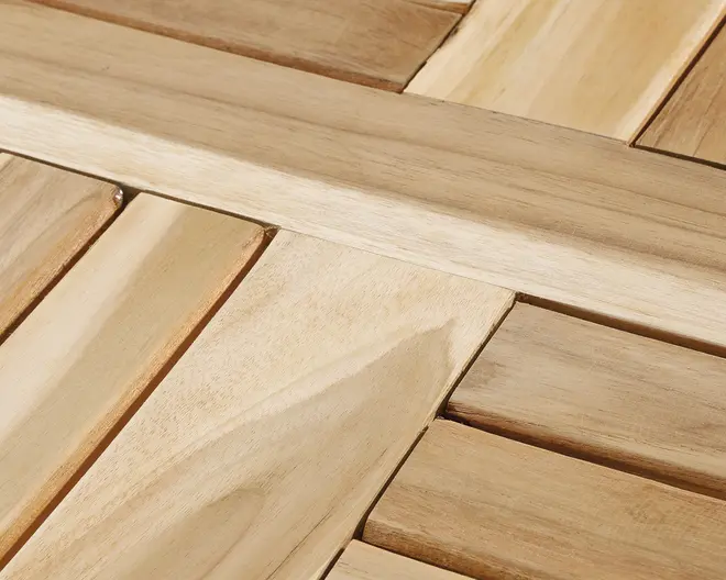 Nærbillede af en træoverflade med sammenlåsende lameller arrangeret i et geometrisk mønster. Træet har en glat finish med synlig naturlig åretegning og varierende lysebrune nuancer, hvilket giver et varmt og naturligt udseende. Konstruktionen virker solid med præcise samlinger og rene kanter.