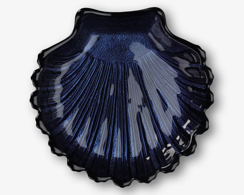 En blank, mørkeblå skål formet som en kammuslingeskal med detaljerede riller og en tekstureret overflade. Kanterne er bølgede, og den skinnende finish giver et elegant og dekorativt udtryk.