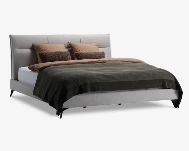 Moderne seng med lysegråt polstret hovedgærde og ramme, kendetegnet ved rene linjer og et minimalistisk design. Sengen er redt med to store lysebrune puder, to mindre teksturerede brune puder, en lysebrun dyne og et mørkegrønt tæppe. Benene er slanke og sorte, hvilket giver sengen et let hævet udseende.