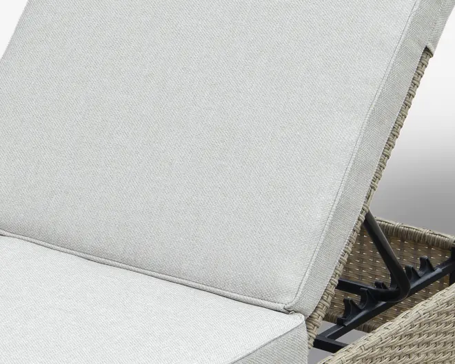 Nærbillede af en lys grå, tekstureret pude med tyk, polstret udformning. Puden er fastgjort til et møbel med en ramme af flet og har en justerbar metalmekanisme til tilbagelæning, som er synlig på siden. Stoffet ser slidstærkt ud og egner sig til udendørs brug.