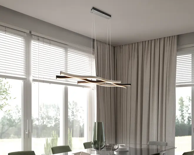 Moderne pendellampe med tre sammenflettede, bølgeformede LED-stænger ophængt fra loftet i tynde, næsten usynlige wirer. Lampen har en elegant sort og gylden finish, der giver et stilrent og eksklusivt udtryk. Designet sikrer jævn lysfordeling og egner sig godt til spise- eller opholdsrum. Lampen hænger over et glasbord og passer perfekt til minimalistiske og moderne indretninger.