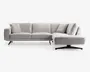 En moderne L-formet sofa med lysegråt betræk, rene linjer og lav profil. Sofaen har tre siddehynder til venstre og en forlænget chaiselong til højre, understøttet af slanke, skrå metalben. Ryglæn og armlæn er polstrede, og sofaen leveres med flere matchende ryg- og sidepuder for ekstra komfort.