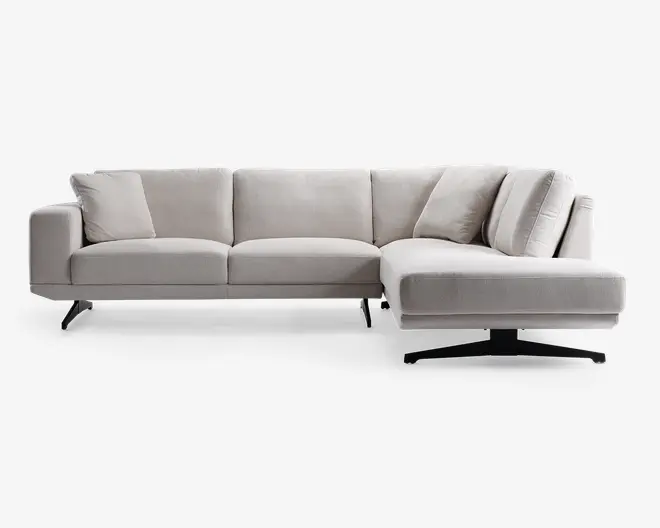 En moderne L-formet sofa med lysegråt betræk, rene linjer og lav profil. Sofaen har tre siddehynder til venstre og en forlænget chaiselong til højre, understøttet af slanke, skrå metalben. Ryglæn og armlæn er polstrede, og sofaen leveres med flere matchende ryg- og sidepuder for ekstra komfort.