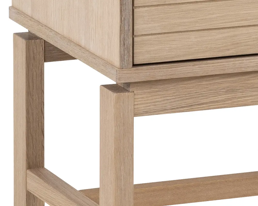 Nærbillede af et møbel i lyst træ med naturlig finish, der har rene, lige linjer og et moderne, minimalistisk design. Benene er firkantede og solide, forbundet med vandrette støtter, og sidepanelet viser en glat, sømløs konstruktion.