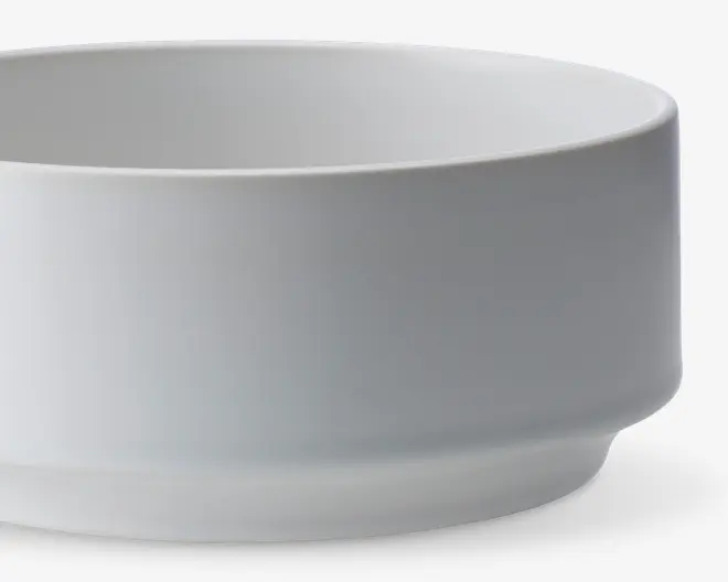 En enkel, hvid keramikskål med en glat, mat overflade. Skålen har lige sider og en let hævet bund, hvilket giver den et moderne og minimalistisk udtryk. Overfladen er uden mønstre, tekstur eller dekorationer.