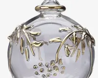 Et klart, rundt glasobjekt med et dekorativt design, der viser guldfarvede grene og blade samt små gyldne bær. De gyldne detaljer er hævede og omkranser overfladen, hvilket giver genstanden et elegant og luksuriøst udseende.