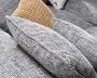 Nærbillede af flere teksturerede, vævede pyntepuder i lysegrå og beige, arrangeret på en grå sofa med blødt, kraftigt stofmønster og spids, rektangulær form.