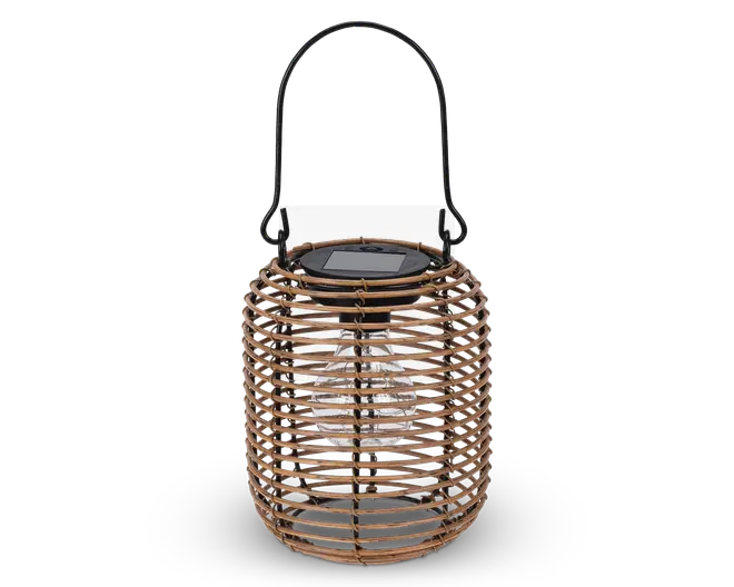 En cylindrisk lanterne med et flettet rattan-ydre og en klar glaspære indeni. Toppen har et sort solpanel til opladning, og der er et solidt sort metalhåndtag fastgjort til nem transport eller ophængning. Designet kombinerer rustikke og moderne elementer og er velegnet til både udendørs og indendørs brug.
