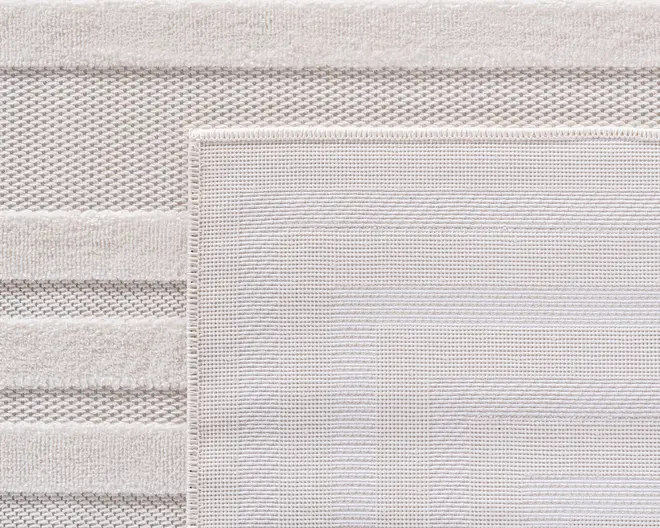 Nærbillede af to overlappende bade måtter i en lys beige farve. Den øverste måtte har et diskret geometrisk mønster med koncentriske rektangler og en pænt syet kant. Måtten nedenunder har skiftevis teksturerede striber, der kombinerer bikubemønster og bløde frottésektioner for ekstra greb og komfort.