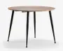 Rundt bord med en lys træbordplade og fire slanke, koniske sorte metalben. Designet er minimalistisk og moderne med en glat overflade og rene linjer, velegnet til moderne indretning.