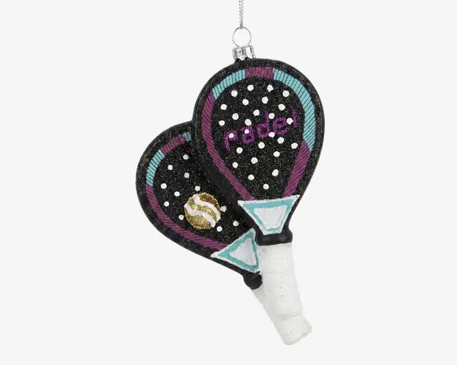 Denne pynt forestiller to overlappende padelbat med sorte flader dekoreret med hvide prikker og farverige detaljer i turkis, lilla og guld. På det ene bat står der 'padel' med lilla glimmer, og mellem battene er der placeret en lille gul og hvid bold. Håndtagene er omviklet med hvidt og har turkise trekantede mønstre nær bunden. Øverst er der en sølvfarvet ophængssnor.