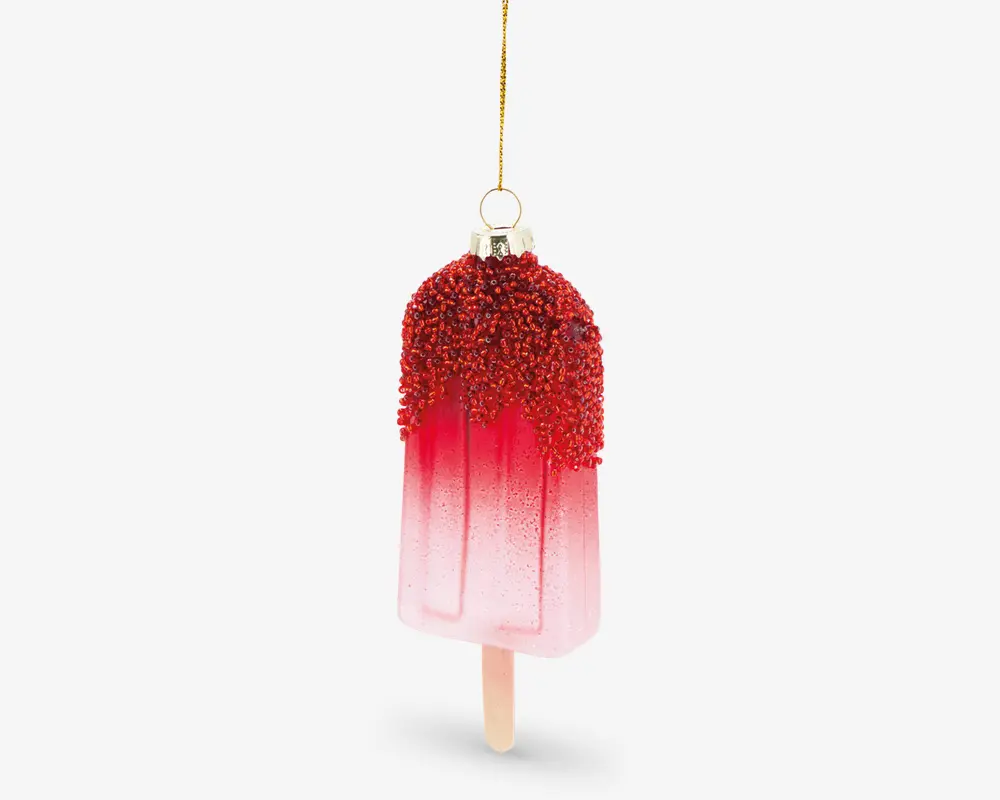 Et dekorativt ornament formet som en ispind, med en farvegradient fra lyserød til rød. Den øverste del er dækket af røde, teksturerede perler, der ligner krymmel eller slik, og ornamentet hænger i en gylden løkke og snor. Ispindens træpind er synlig i bunden, hvilket giver et realistisk udseende.