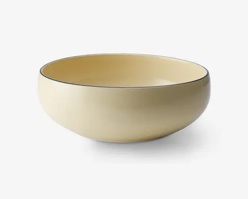 En rund skål med glatte sider og blank, lysebeige overflade både indvendigt og udvendigt. Skålens kant er markeret med en tynd, mørk streg, som giver et diskret og elegant udtryk. Skålen har et minimalistisk design uden hanke eller mønstre og egner sig til servering af forskellige retter.