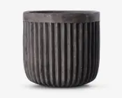 En rund, mørkegrå potte med mat finish og lodrette riller, der løber fra bunden op til lige under kanten. Kanten er glat og en smule tykkere end resten af potten, hvilket giver et moderne og industrielt udtryk.