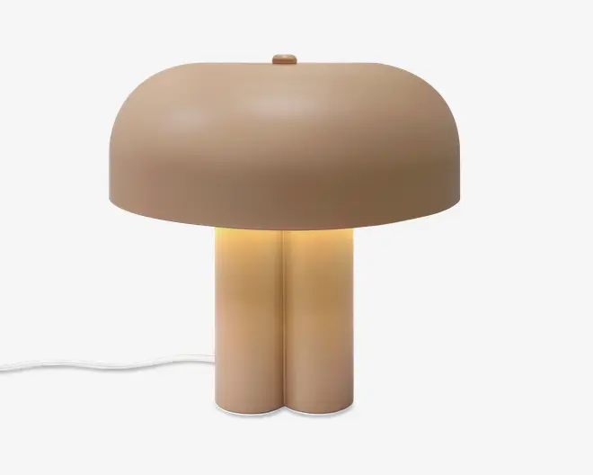 En beige svampeformet lampe med rund kuppelformet skærm, varmt lys i midten og en glat todelt fod med en hvid ledning, der går ud til siden.