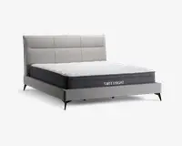 Moderne seng med et lysegråt polstret hovedgærde med rektangulære paneldetaljer, matchende polstret ramme og slanke sorte ben. Madrassen er middeltyk med hvid quiltet top og mørkegrå sider, hvor mærket 'SWEETNIGHT' er vist på siden.